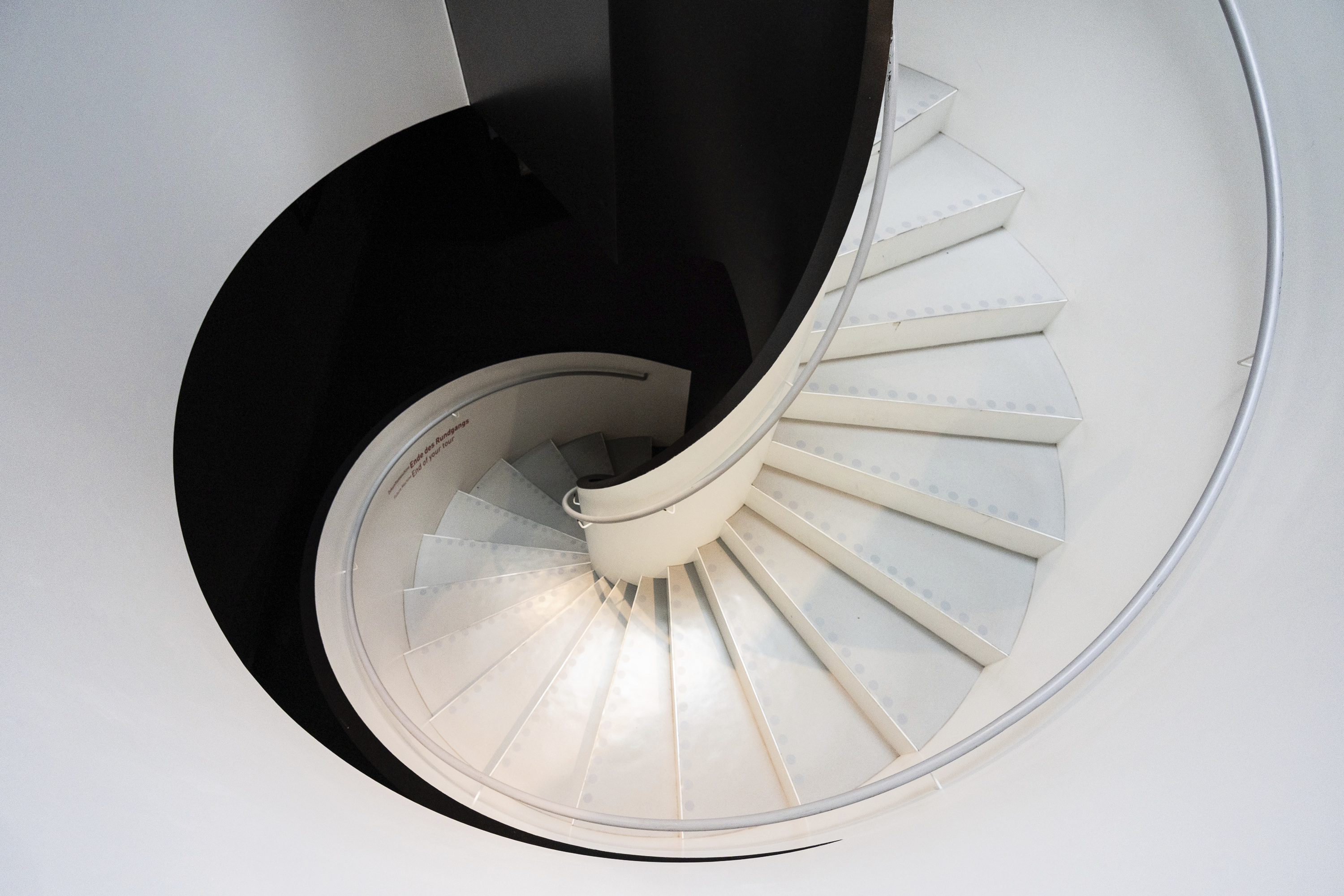 High-angle view of a spiralling black and white staircase looking like a pearlescent shell at Futurium Berlin.