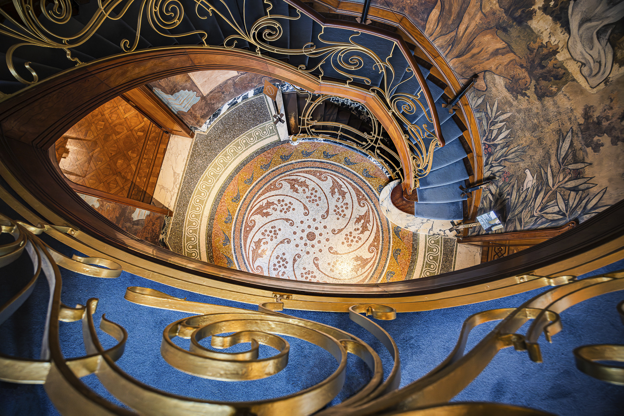 High-angle view of the magnificent art nouveau staircase at Maison Hannon in Brussels. Those stairs feature intricate wrought-iron railings and are adorned with captivating frescoes, creating a stunning and immersive atmosphere. Below the stairs, a striking mosaic adds to the opulent design.
Maison Hannon was designed by architect Jules Brunfaut and constructed between 1903 and 1904.