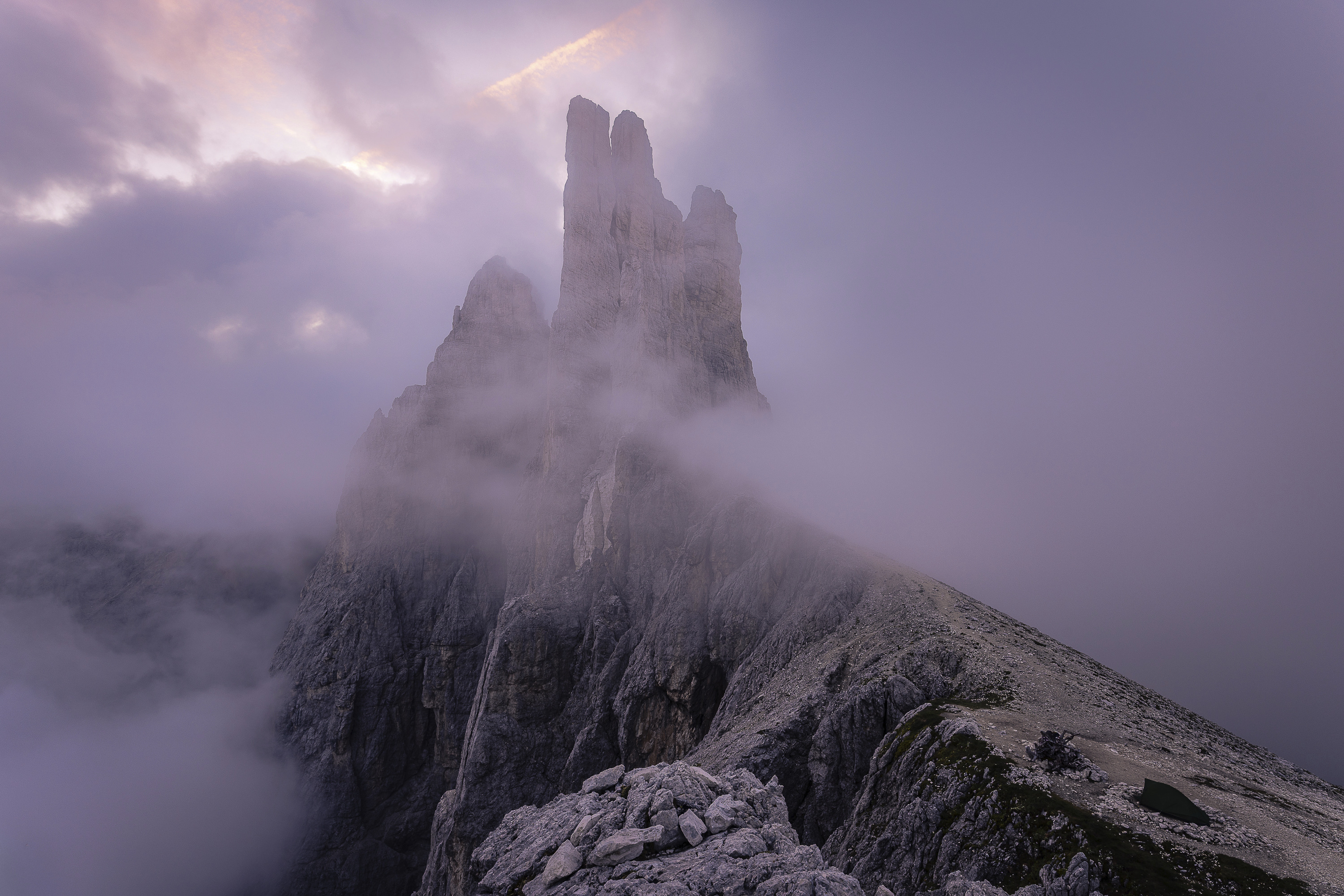 Foggy sunset at Vajolet rocky towers in the Dolomites. Mountain pointy picks raise above the fog in a purple light.